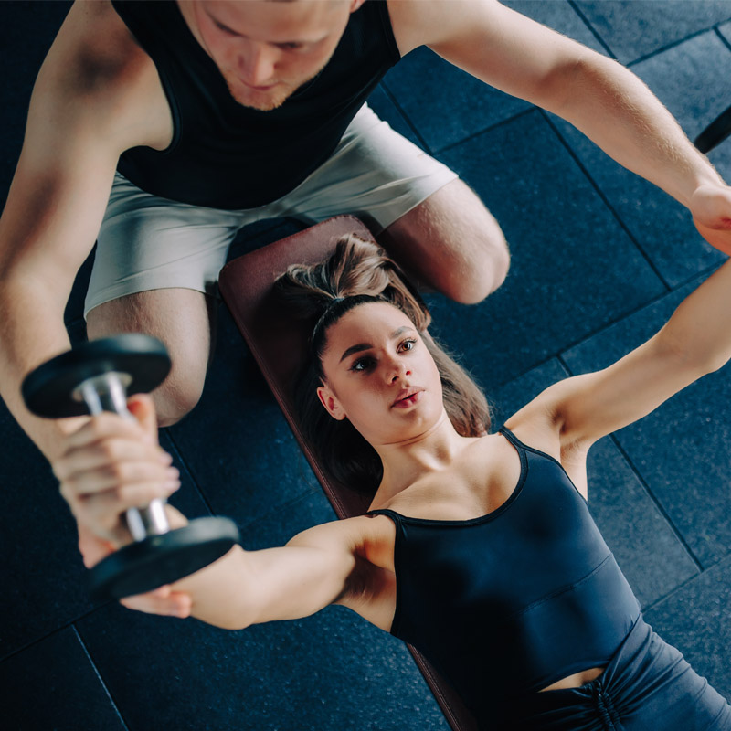 Sportfysiotherapeut begeleidt vrouw bij krachtraining met dumbbells.