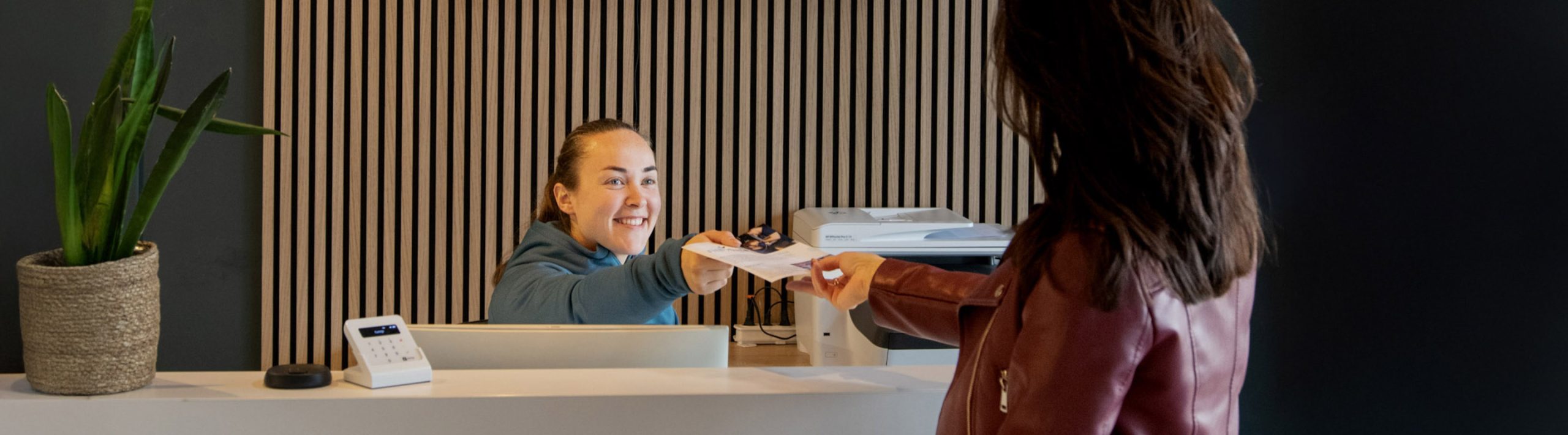 Vrouw achter de balie van Joint Care fysiotherapie helpt een patiënt.