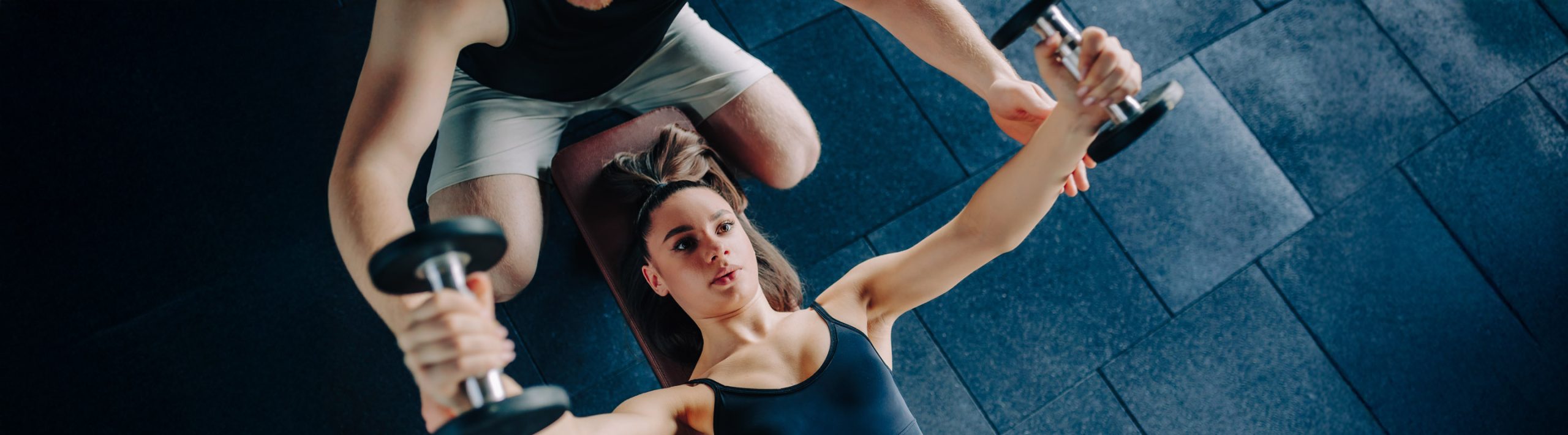 Vrouw doet krachtoefeningen met dumbbells onder toezicht van een fysiotherapeut voor revalidatie.