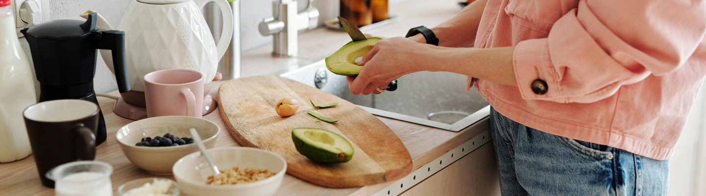 Vrouw bereidt een gezond ontbijt met havermout, blauwe bessen en avocado.