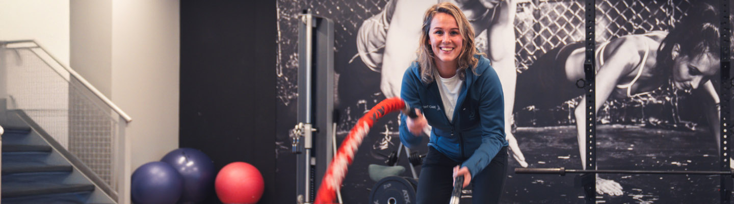 Vrouw in blauw vest traint met battle ropes bij Joint.Care